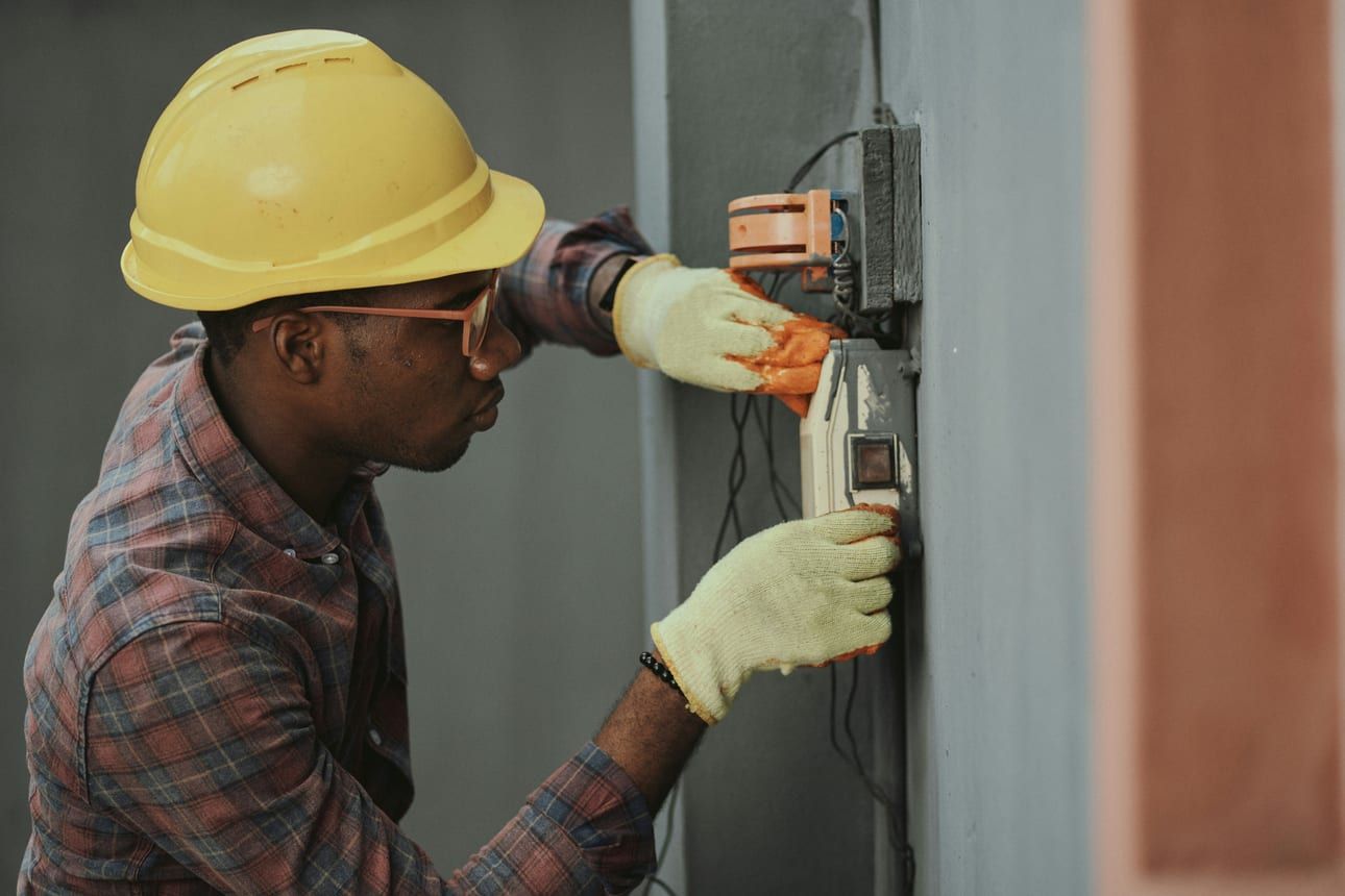 A Circle City electrician in a hard hat and work gloves working on an electrical panel.