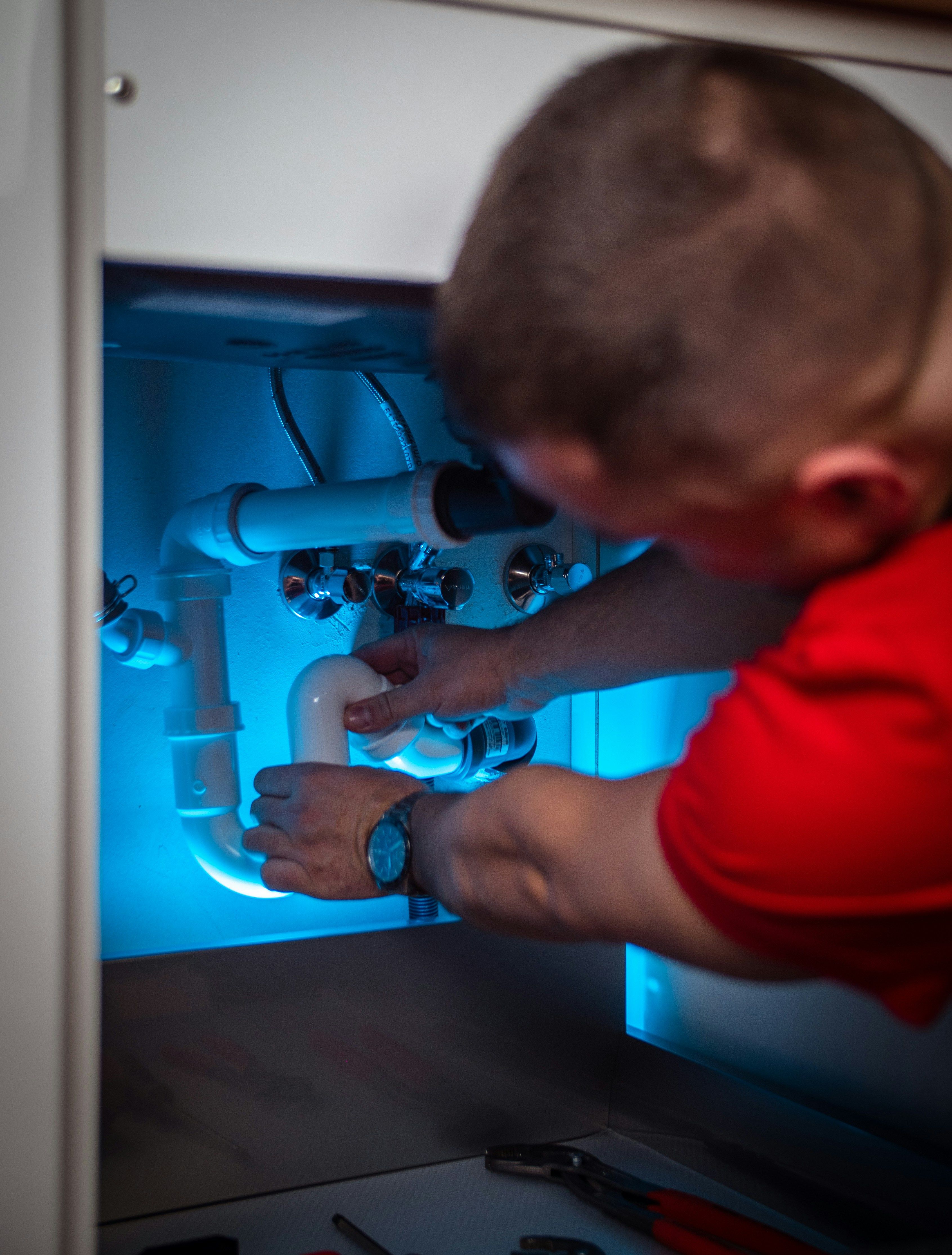 A Circle City plumber working on the pipes beneath a kitchen sink.