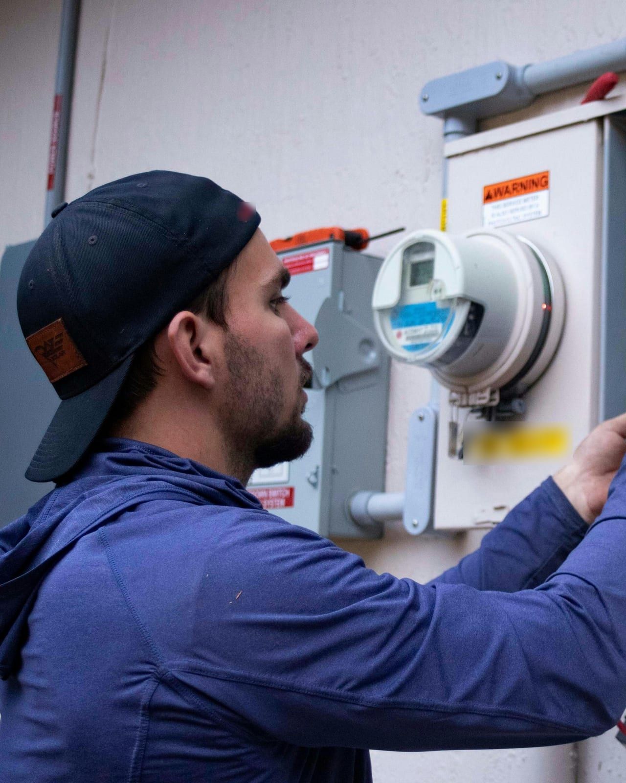 A Circle City technician in a ballcap working on an outdoor residential electrical meter and panel.